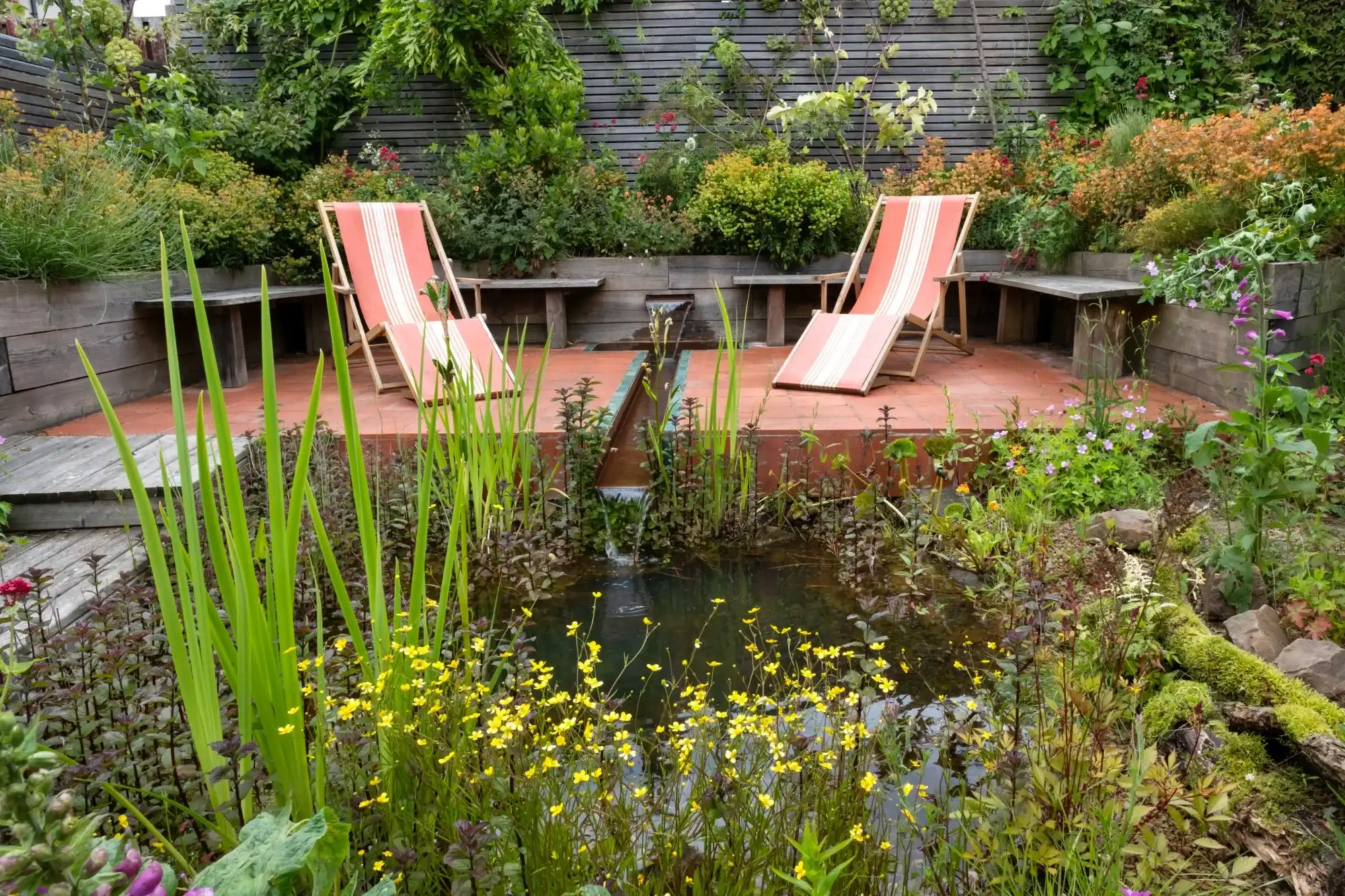 Terracotta patio with striped deckchairs beside the corten steel rill and sleeper seating