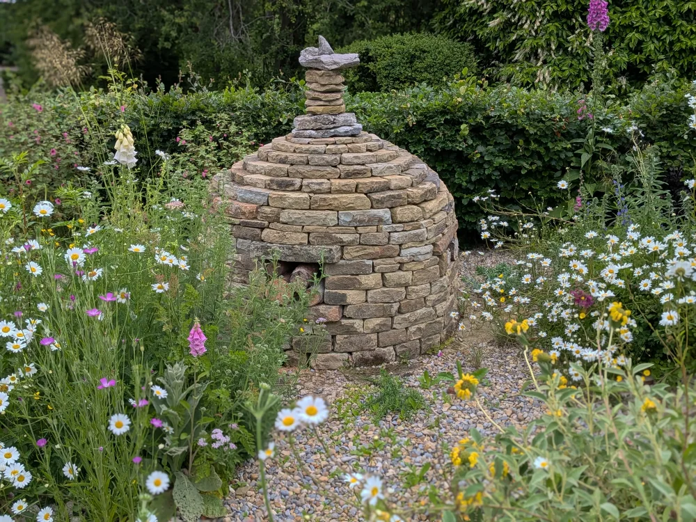 Drystone stupa surrounded by oxeye daisies, foxgloves and gravel planting in The Water Garden