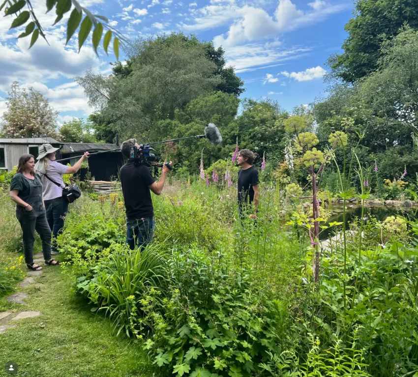 BBC Gardeners' World film crew interviewing Will Tomson in his wildlife garden among foxgloves and tall planting beside the pond
